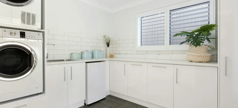 Modern tvättstuga med vita skåp, staplad tvättmaskin och torktumlare samt gott om bänkyta